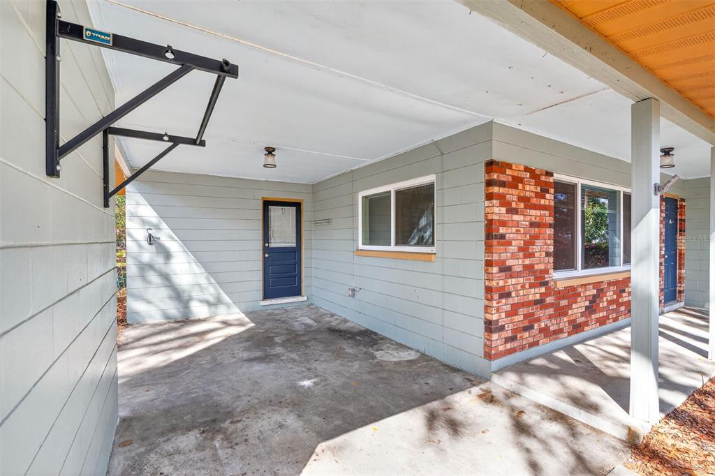 A covered concrete patio features light green siding, a brick accent wall, and a pull-up bar — 2200 NE 16TH TERRACE, GAINESVILLE, FL
