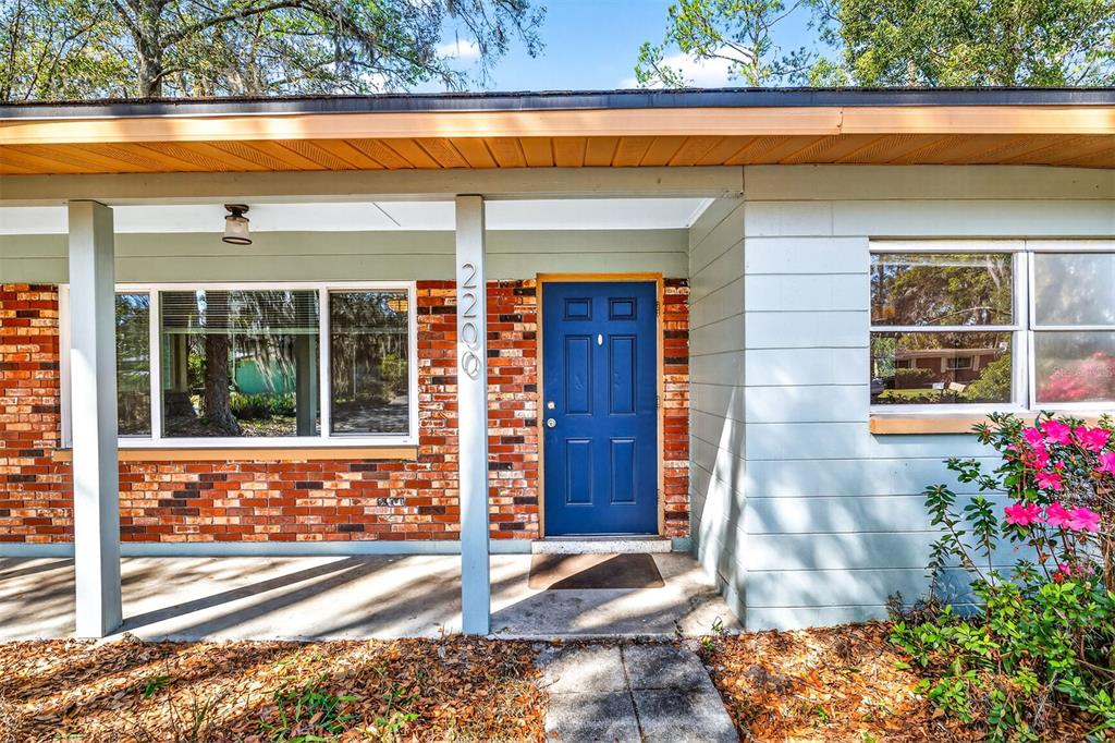 A blue front door is centered between a brick facade and light blue siding — 2200 NE 16TH TERRACE, GAINESVILLE, FL