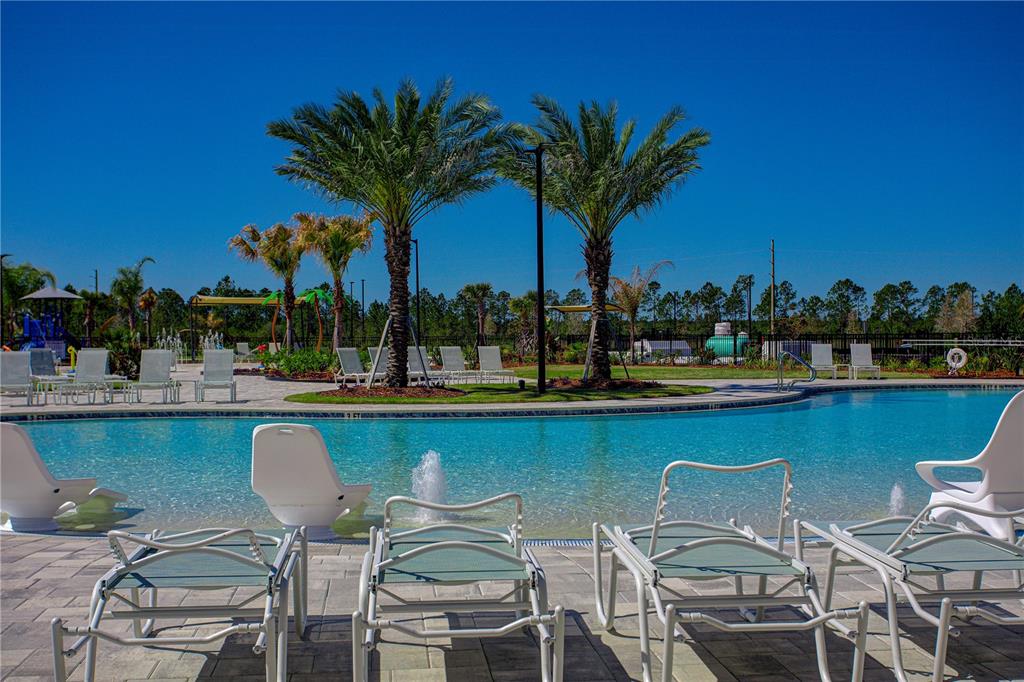 A swimming pool with lounge chairs and palm trees under a clear blue sky — 21 HULETT WOODS ROAD, PALM COAST, FL