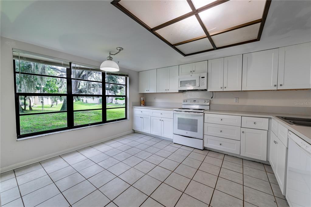 A kitchen with white cabinets, white appliances, tiled floors, and a large window overlooking trees — 7873 NIAGARA AVENUE UNIT 1803, TAMPA, FL