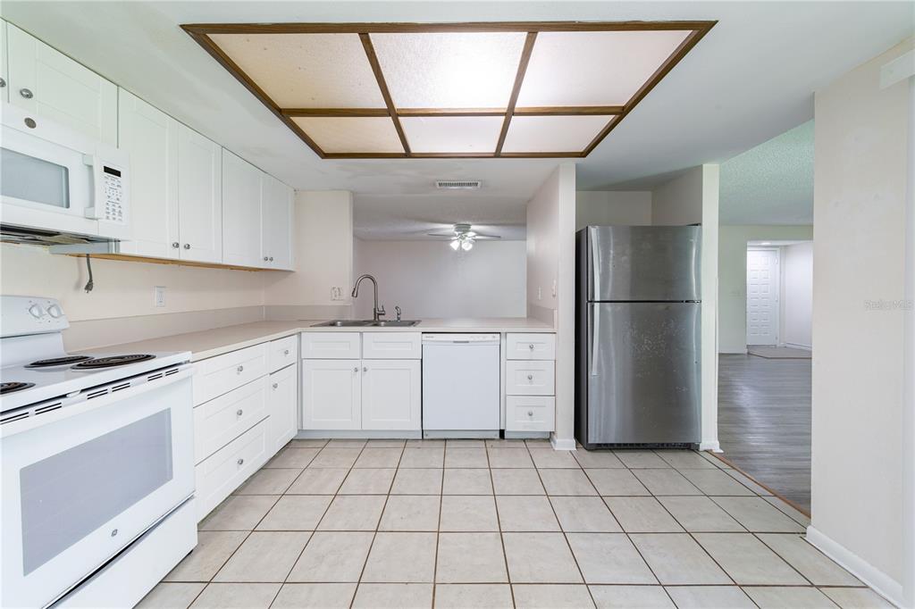 A kitchen with white cabinets, stainless steel refrigerator, white appliances, and a tiled floor — 7873 NIAGARA AVENUE UNIT 1803, TAMPA, FL
