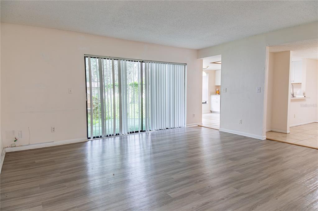 An empty living room features light wood-look flooring, white walls, and a sliding glass door — 7873 NIAGARA AVENUE UNIT 1803, TAMPA, FL