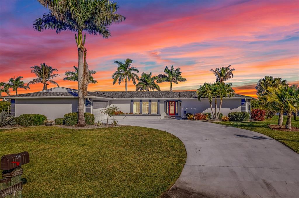 A single-story house with a red front door and palm trees under a sunset sky — 138 COLONIAL STREET SW, PORT CHARLOTTE, FL