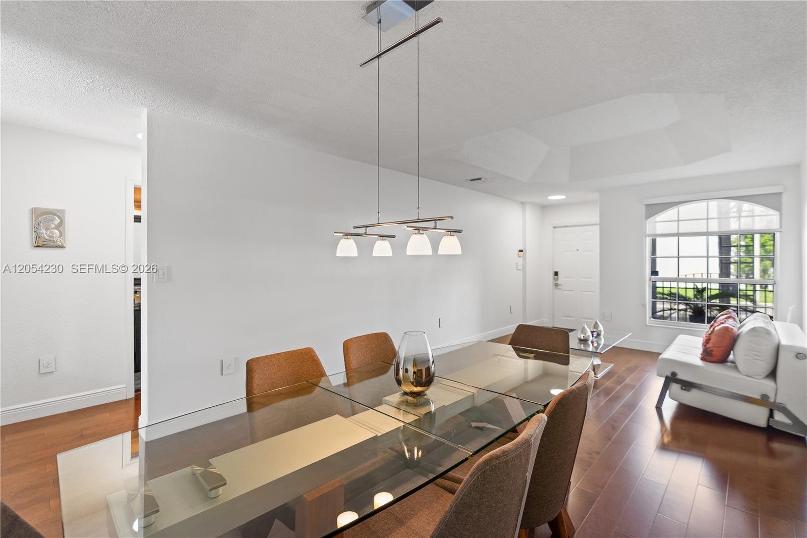 A dining area features a glass-topped table, modern pendant lighting, and hardwood flooring — 5115 NW 116th Ave, Doral FL 33178, DORAL, FL