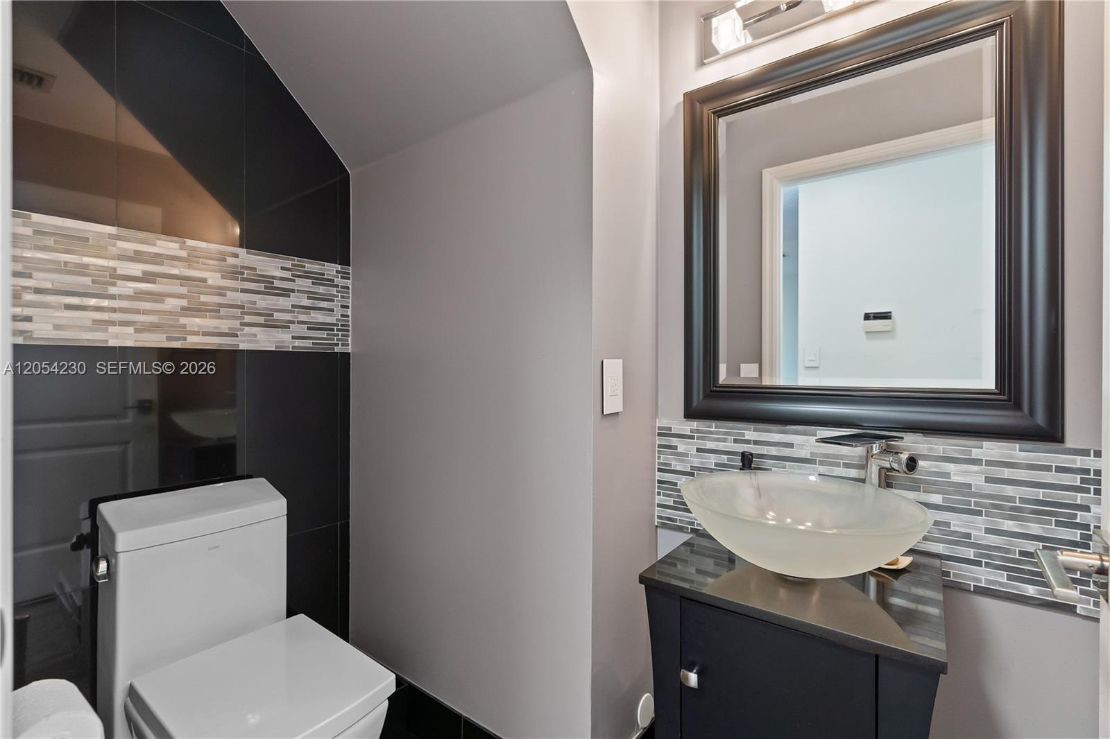 A modern bathroom features a vessel sink, dark vanity, black tile wall, and gray paint — 5115 NW 116th Ave, Doral FL 33178, DORAL, FL