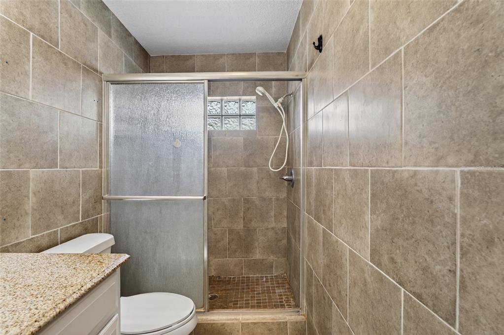 A bathroom features a tiled walk-in shower with a glass door and a granite vanity — 540 W COLUMBIA STREET, LAKE ALFRED, FL