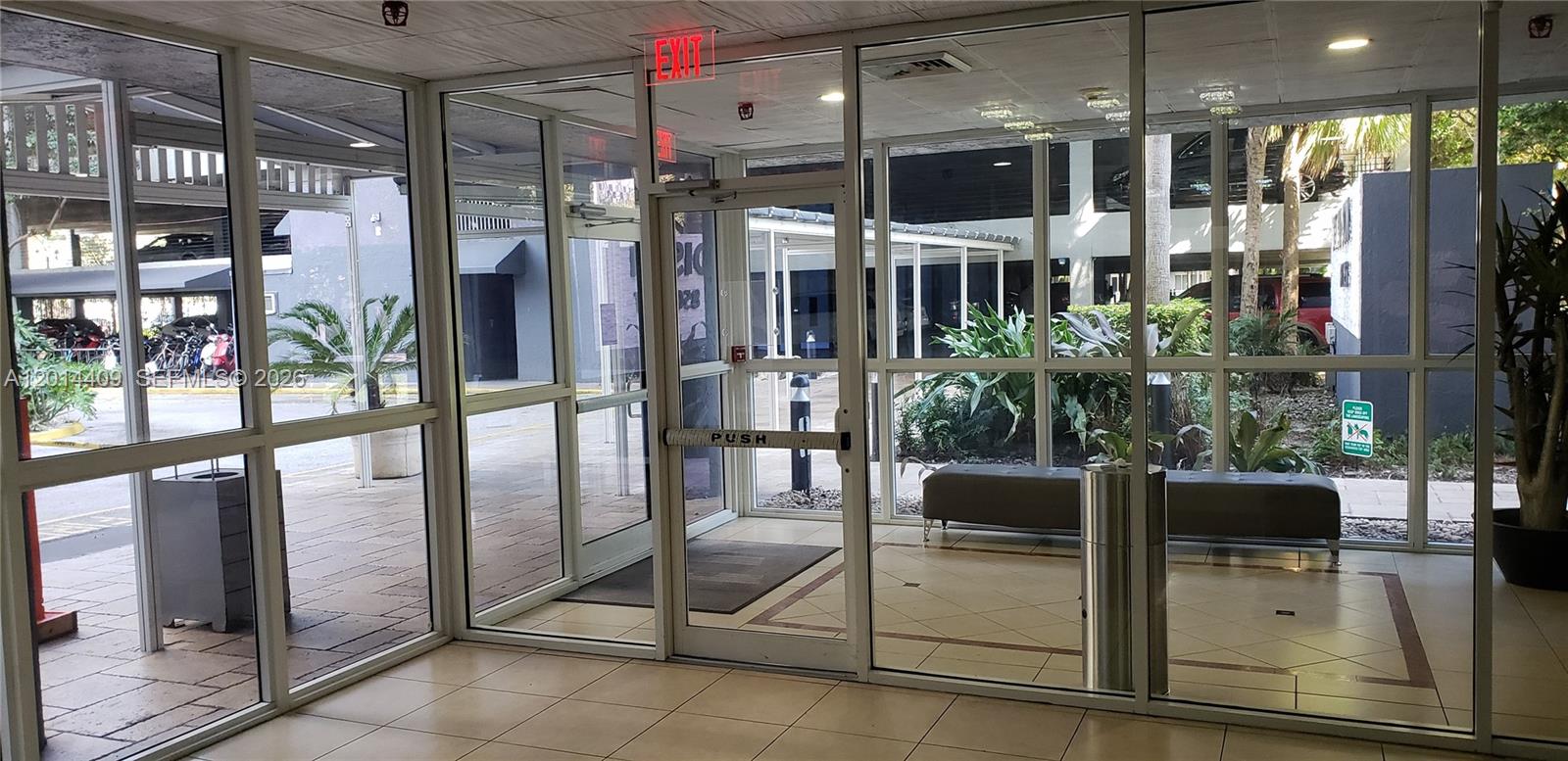 A glass-walled lobby entrance features tile flooring, a push-bar door, and a view of an exterior parking area — 850 N Miami Ave # 903, Miami FL 33136, MIAMI, FL