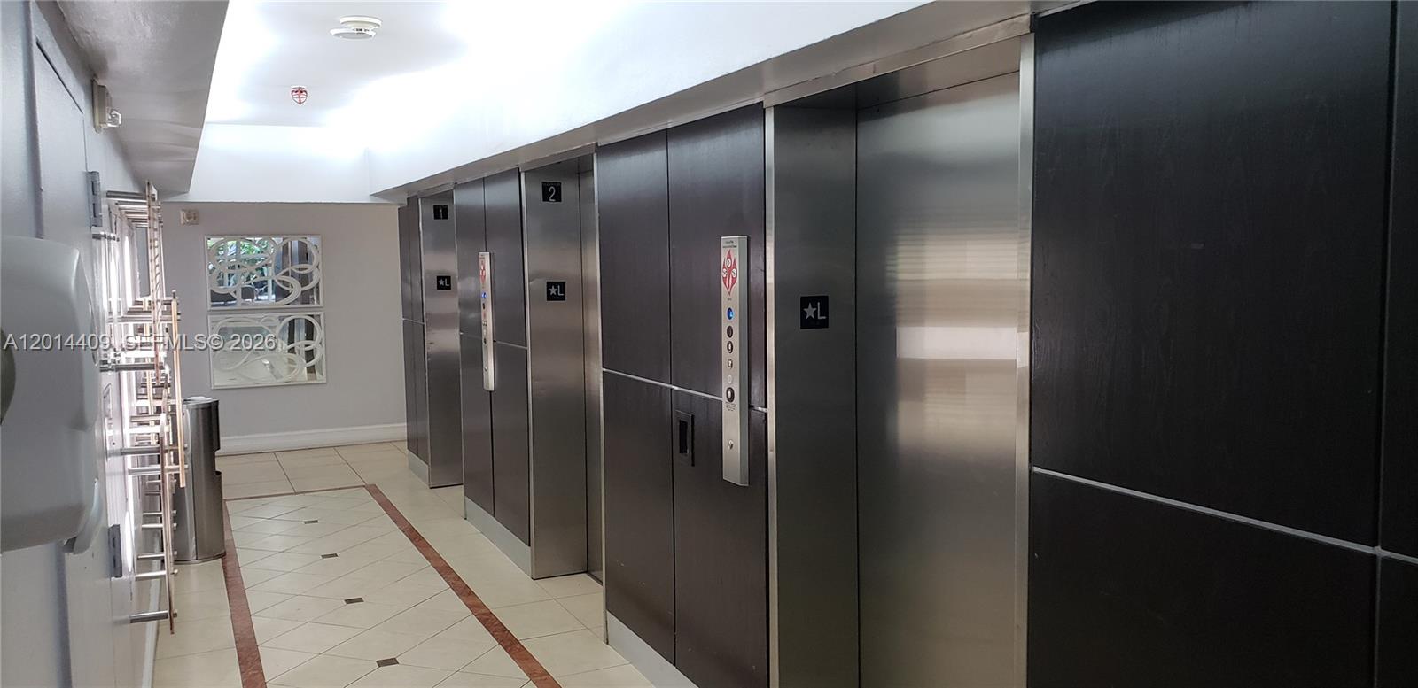A hallway features a row of stainless steel elevator doors with dark wood paneling — 850 N Miami Ave # 903, Miami FL 33136, MIAMI, FL