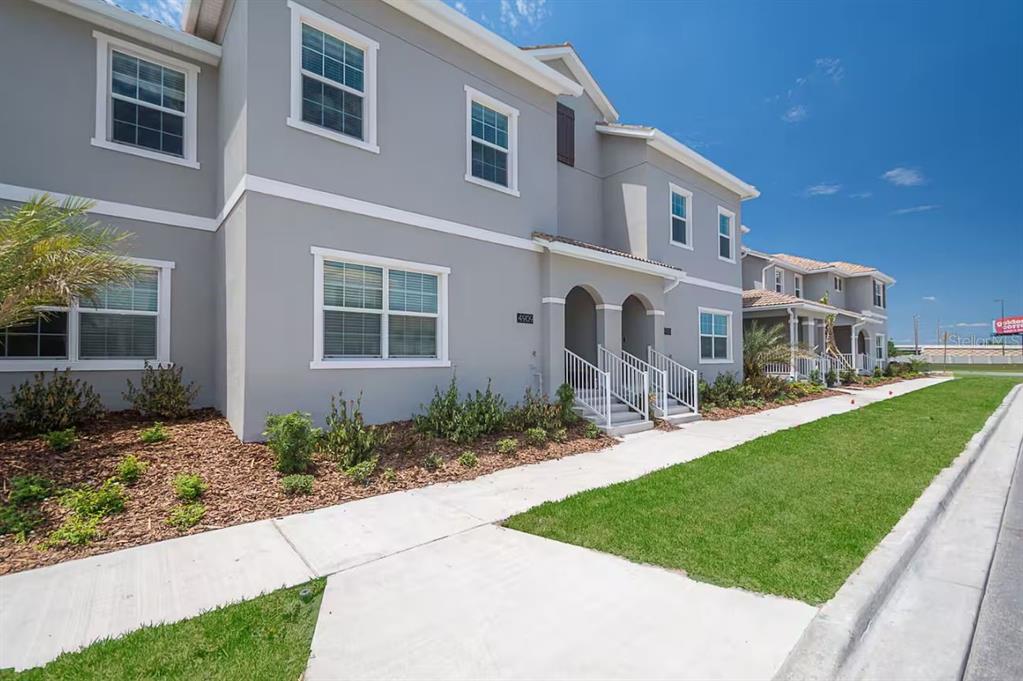 A two-story gray townhouse with white trim, a front walkway, and a manicured lawn — 4909 WINDERMERE AVENUE, KISSIMMEE, FL