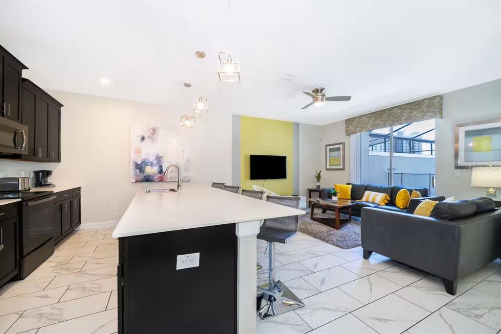 A modern open-concept kitchen and living room with dark cabinets, white countertops, and tile flooring — 4909 WINDERMERE AVENUE, KISSIMMEE, FL