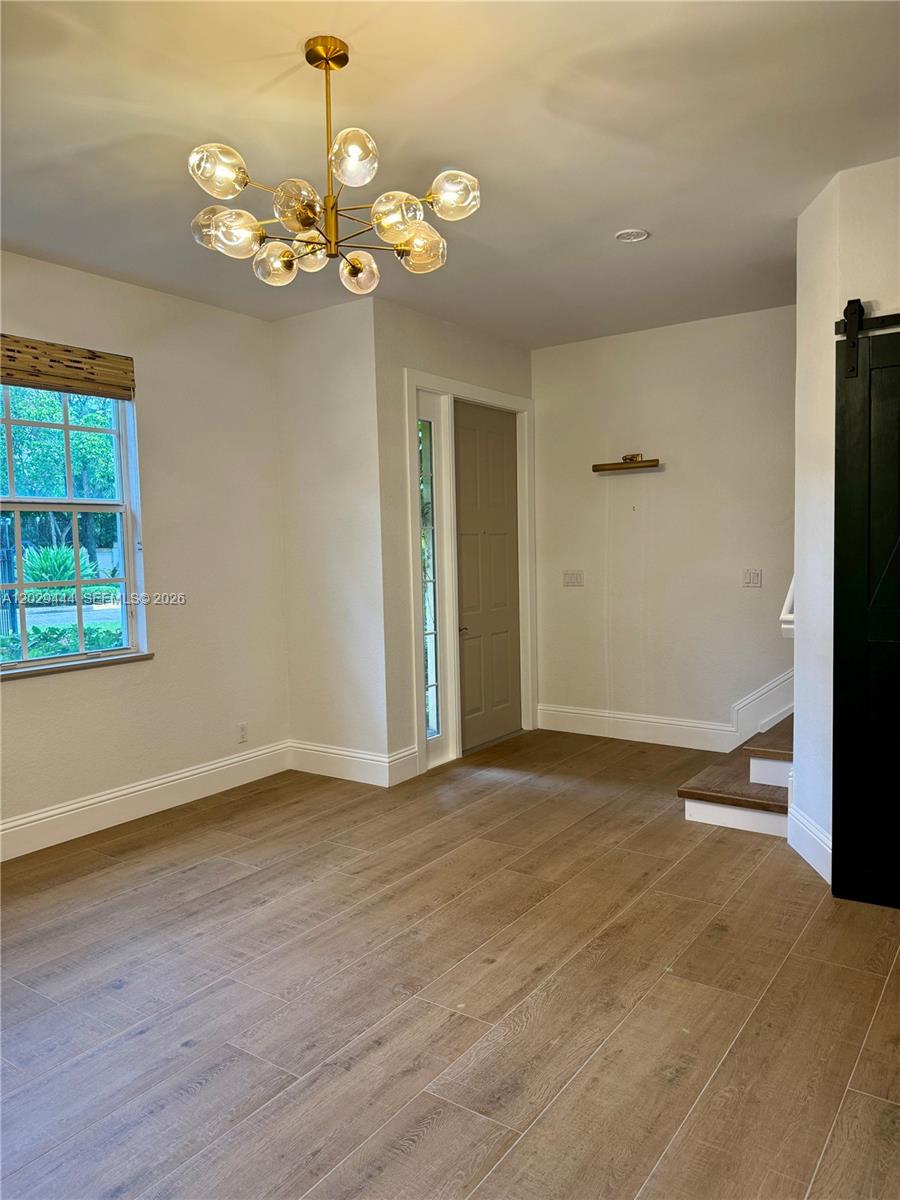 A room with wood-look tile flooring, a modern globe chandelier, and a sliding barn door — 1873 NW 12th St, Boca Raton FL 33486, BOCA RATON, FL