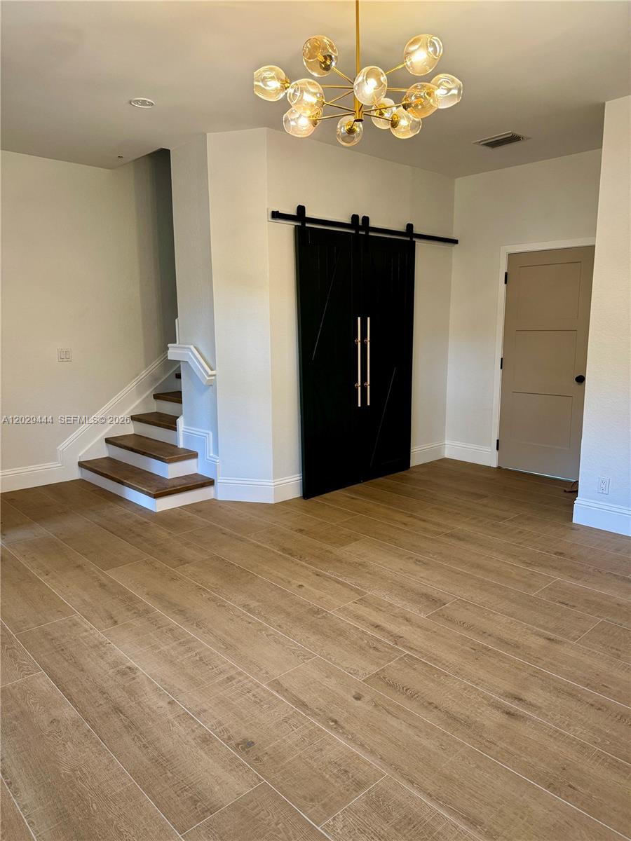 A room features wood-look tile flooring, a staircase, a black sliding barn door, and a chandelier — 1873 NW 12th St, Boca Raton FL 33486, BOCA RATON, FL