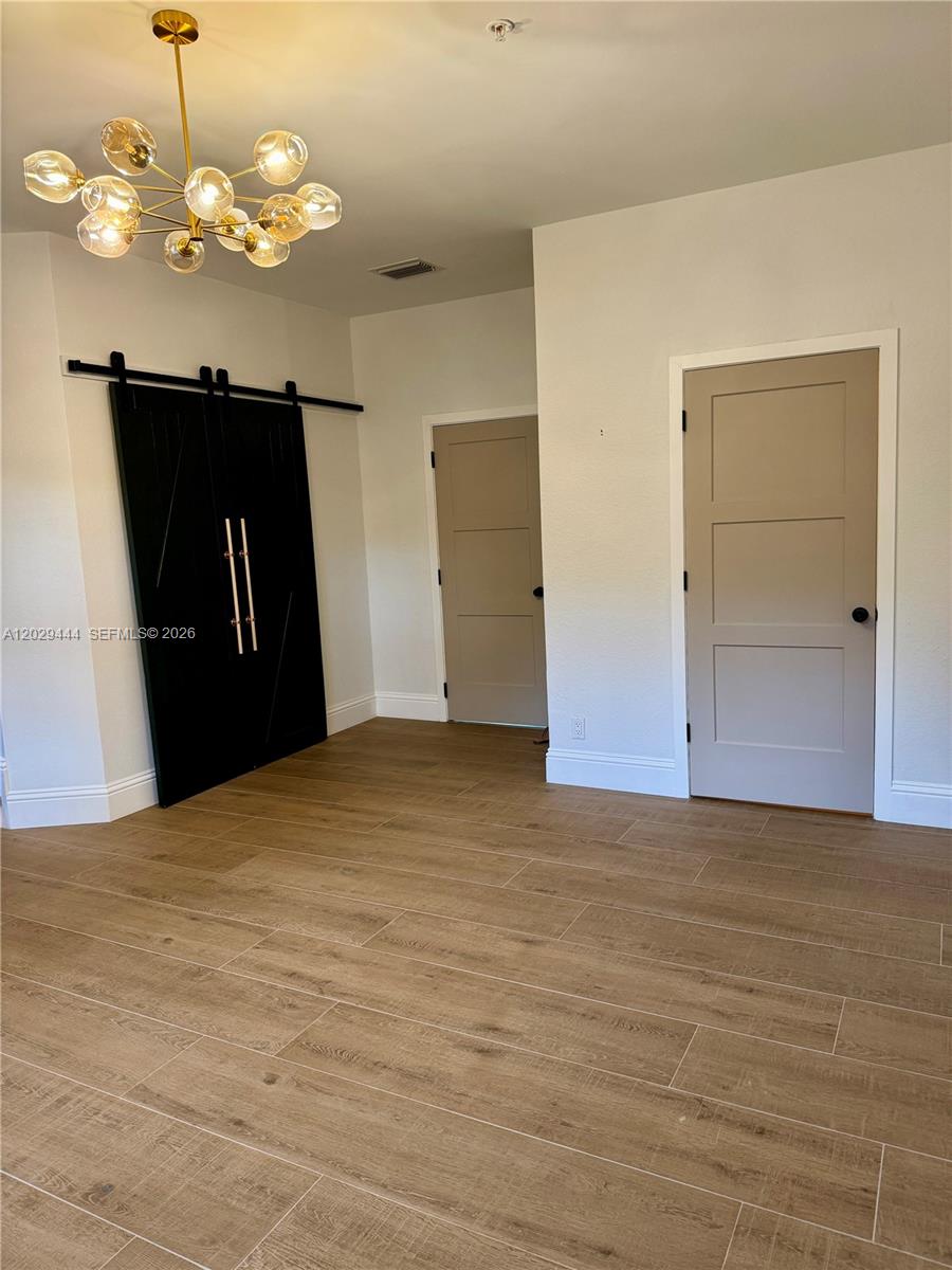 A room features light wood-look tile flooring, a modern gold chandelier, and black barn doors — 1873 NW 12th St, Boca Raton FL 33486, BOCA RATON, FL