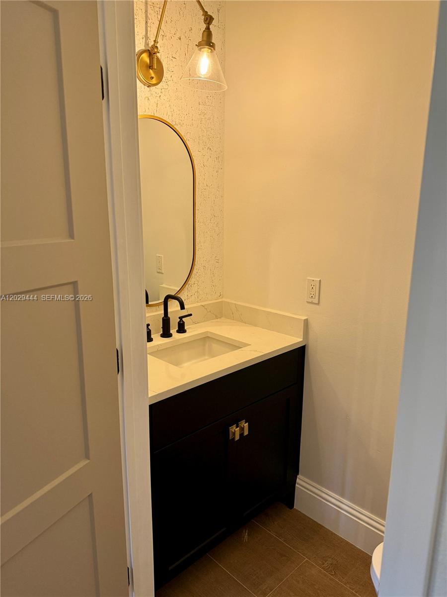 A small bathroom features a dark vanity, white countertop, oval mirror, and patterned wallpaper — 1873 NW 12th St, Boca Raton FL 33486, BOCA RATON, FL