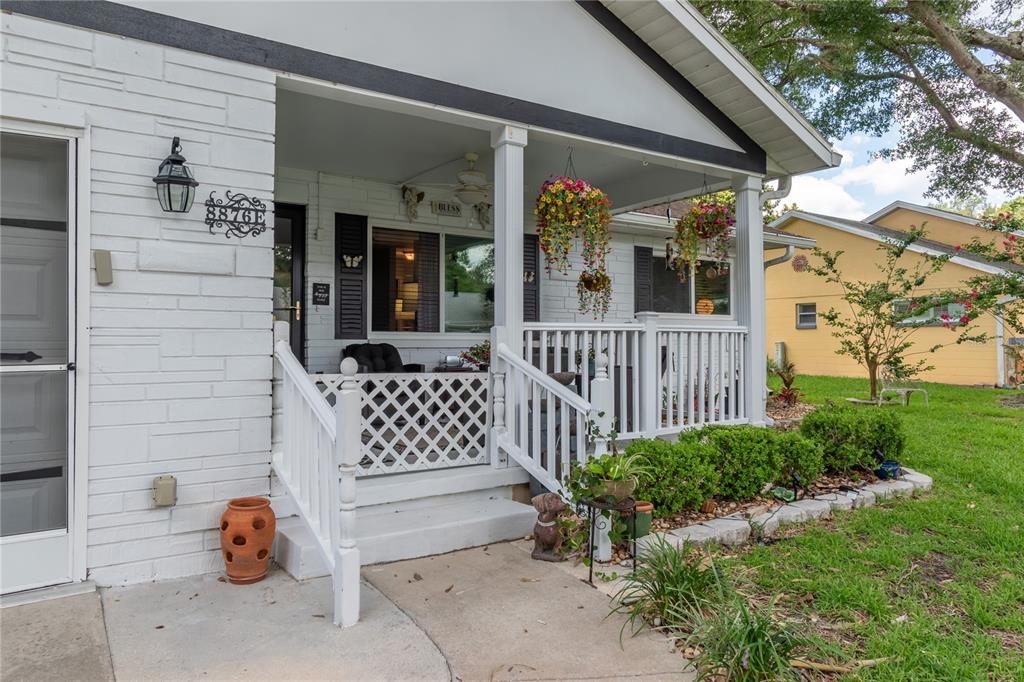A white brick house features a covered front porch with a white railing and hanging plants — 8876 SW 95TH LANE UNIT E, OCALA, FL