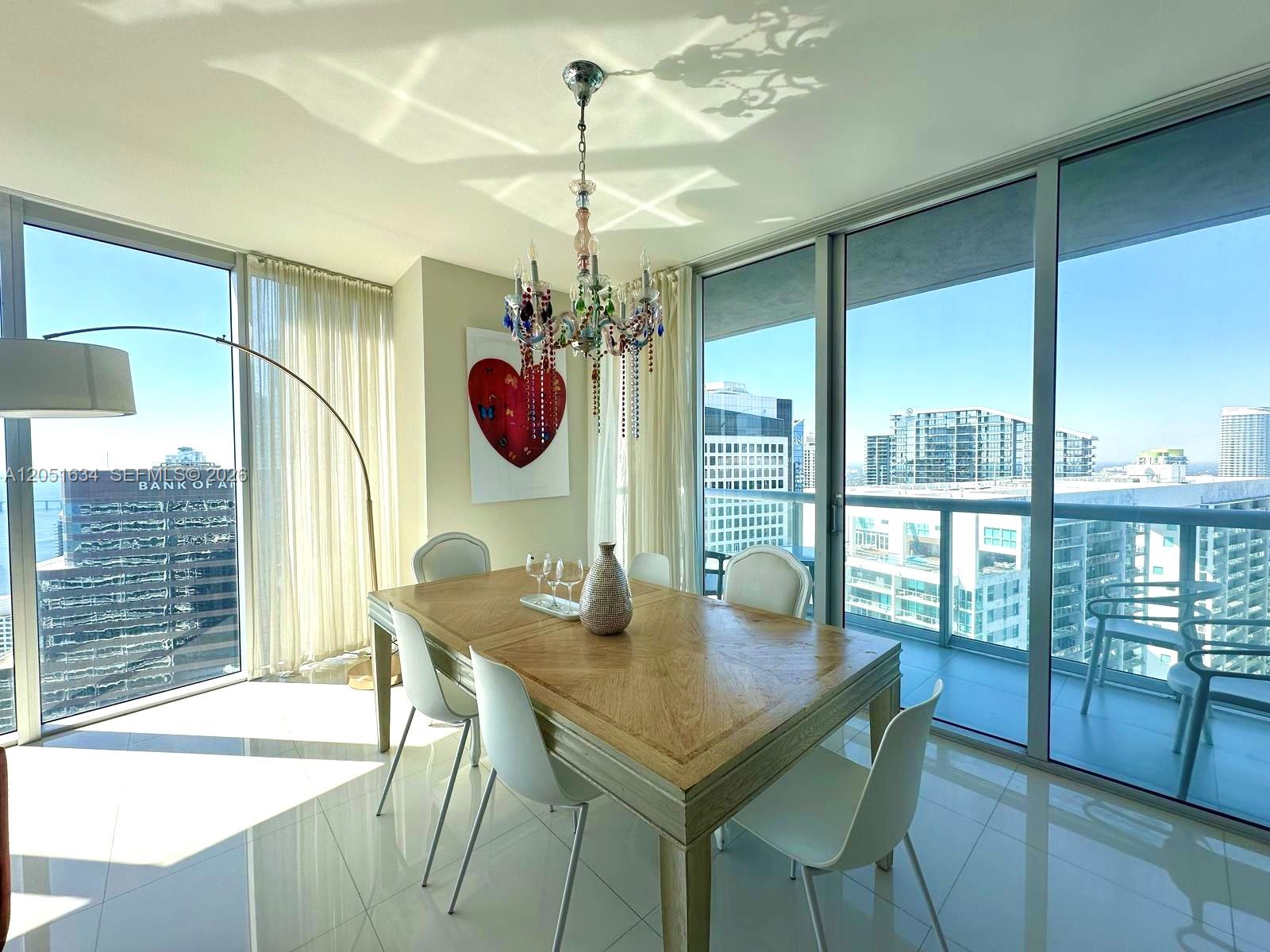 A dining room features a wooden table, white chairs, a colorful chandelier, and floor-to-ceiling windows — 485 Brickell Ave # 4408, Miami FL 33131, MIAMI, FL