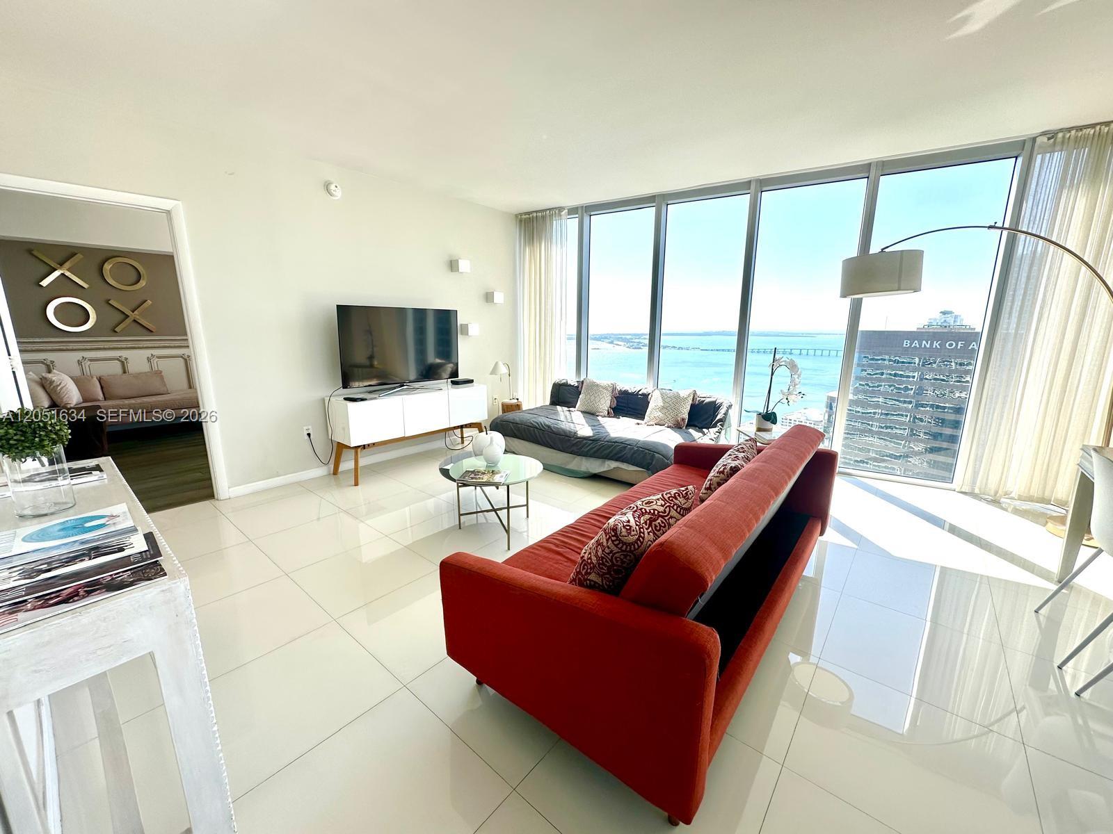 A living room features white tile floors, a red sofa, and floor-to-ceiling windows with water views — 485 Brickell Ave # 4408, Miami FL 33131, MIAMI, FL