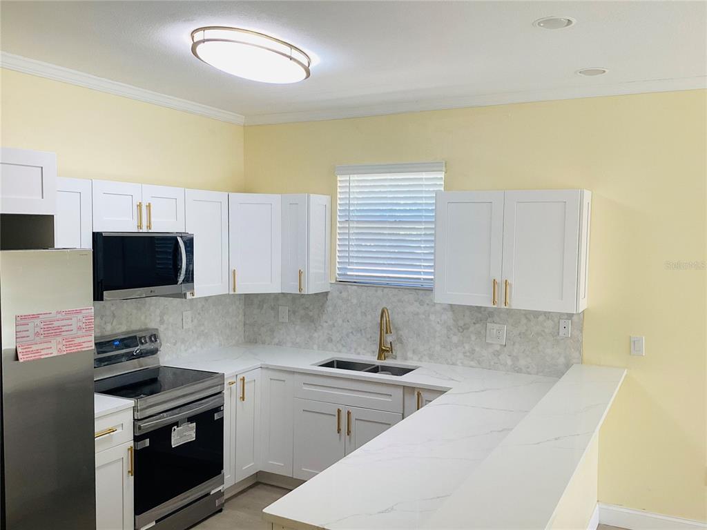 A kitchen features white cabinets, stainless steel appliances, and a white marble-look countertop — 3809 N WHITTIER STREET, TAMPA, FL