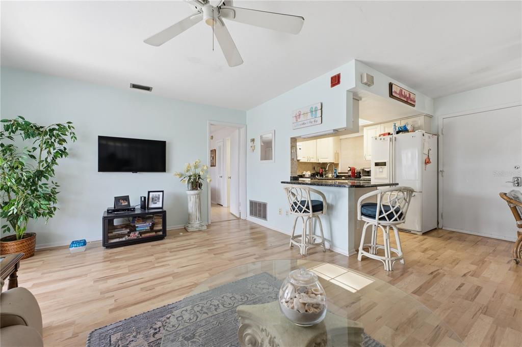 A living room with light wood floors, a ceiling fan, and a kitchen breakfast bar — 3755 S SCHOOL AVENUE UNIT 41, SARASOTA, FL