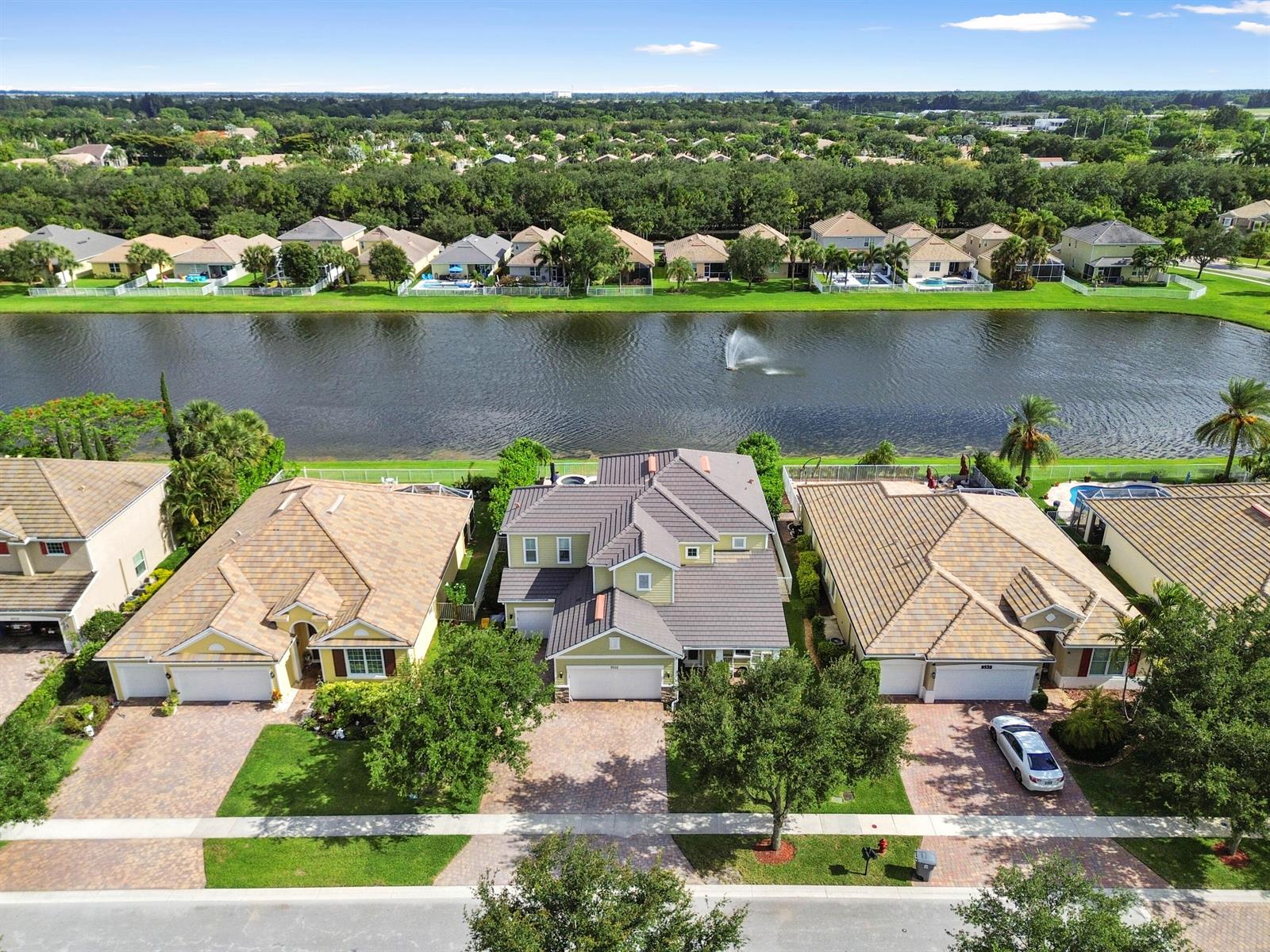 An aerial view shows three suburban houses with tiled roofs facing a lake with fountains — 9526 Wrangler Drive, Lake Worth FL 33467, LAKE WORTH, FL