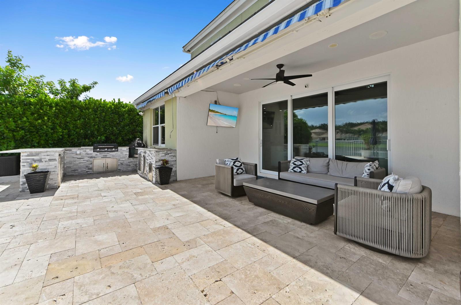 A covered patio features stone flooring, an outdoor kitchen, and a seating area with furniture — 9526 Wrangler Drive, Lake Worth FL 33467, LAKE WORTH, FL