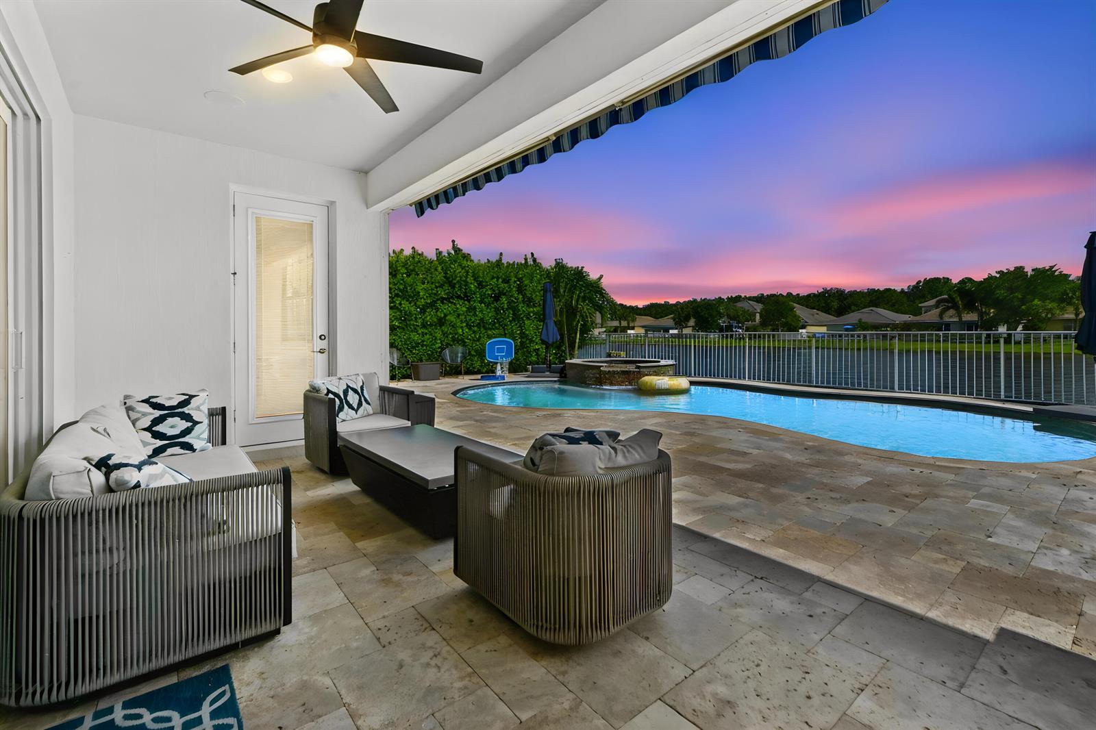 A covered patio features outdoor seating, a stone floor, and a pool overlooking a lake — 9526 Wrangler Drive, Lake Worth FL 33467, LAKE WORTH, FL