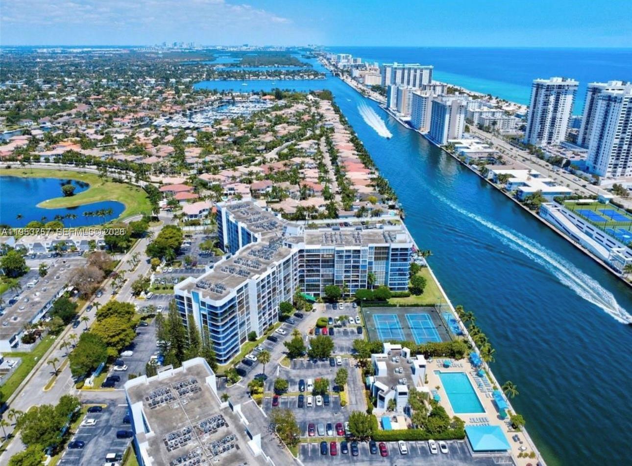 Aerial view of a waterfront condominium complex with a pool, tennis courts, and boat canal — 1000 Parkview Dr # 528, Hallandale Beach FL 33009, HALLANDALE BEACH, FL