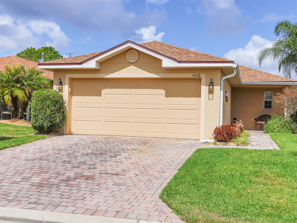 A single-story house with a tan stucco exterior, a two-car garage, and a paved driveway — 4432 TURNBERRY LANE, LAKE WALES, FL