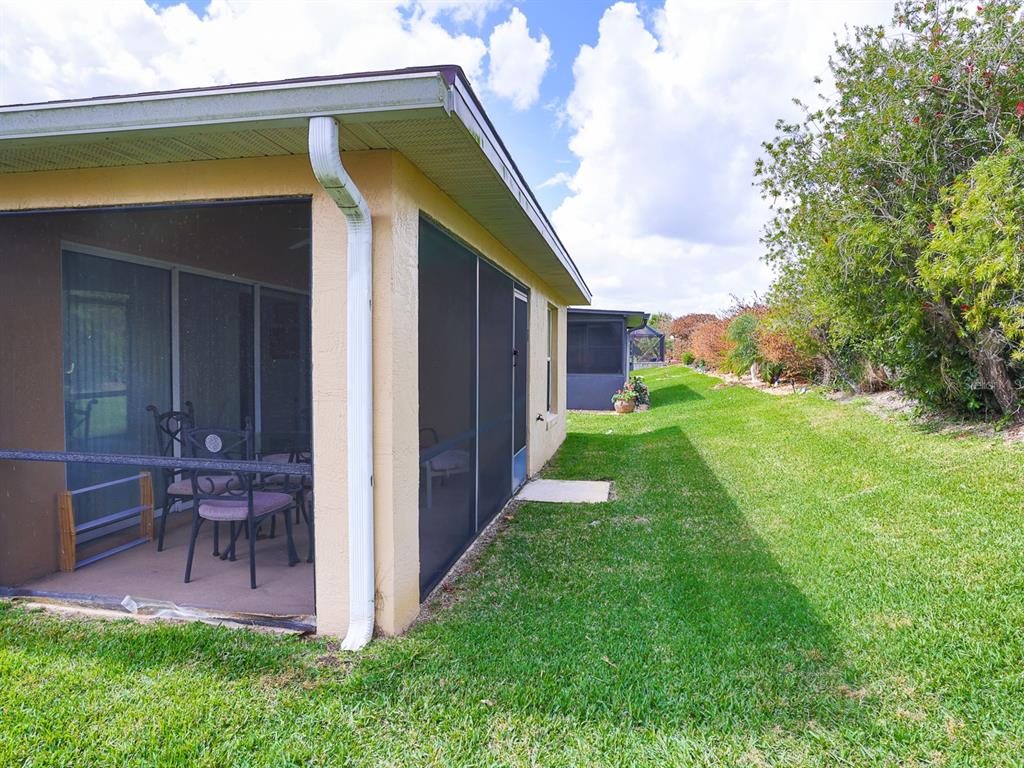 A screened-in patio with outdoor furniture sits beside a grassy yard under a blue sky — 4432 TURNBERRY LANE, LAKE WALES, FL