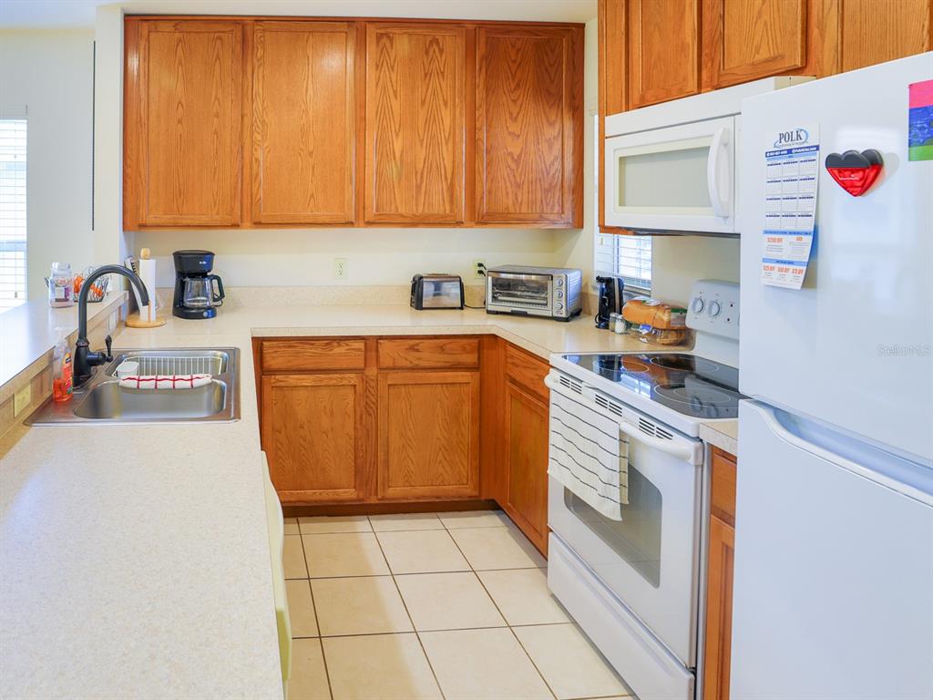 A kitchen features wood cabinets, white appliances, a double sink, and light-colored countertops — 4432 TURNBERRY LANE, LAKE WALES, FL