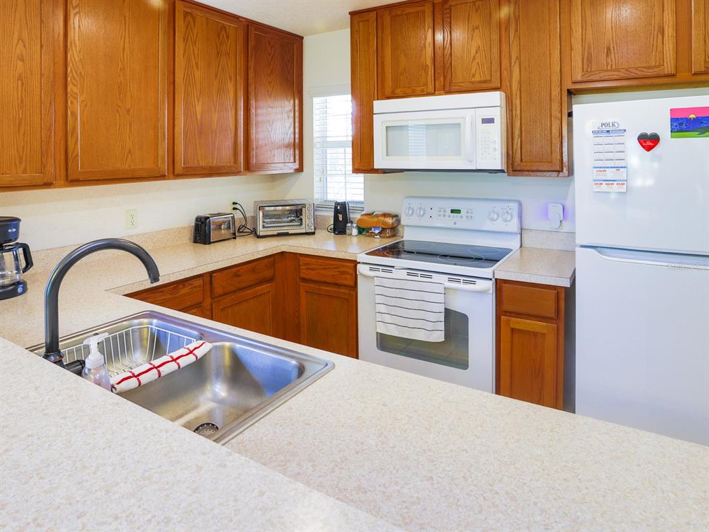 A kitchen features wood cabinets, a white stove, a microwave, and a stainless steel sink — 4432 TURNBERRY LANE, LAKE WALES, FL