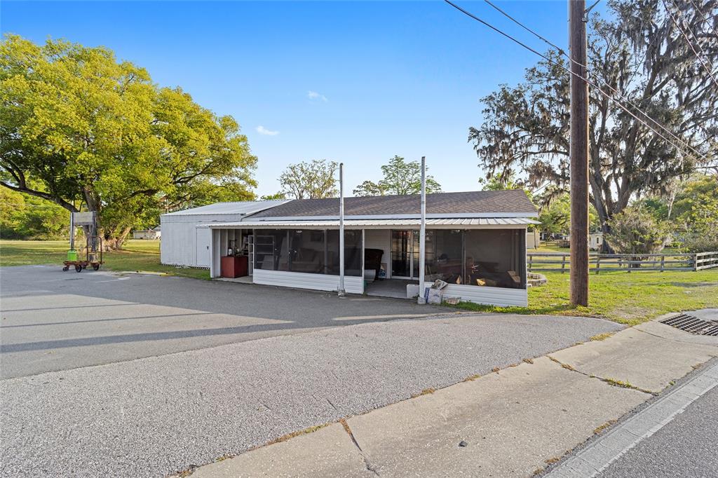A single-story building with a screened-in porch sits next to a large tree and parking area — 6221 SE 110TH STREET, BELLEVIEW, FL
