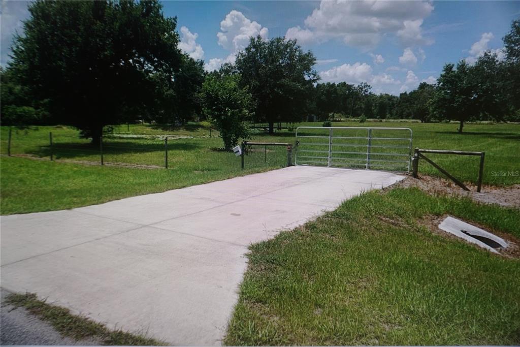 A concrete driveway leads to a metal gate opening into a large, grassy field — 40906 11TH AVENUE E, MYAKKA CITY, FL