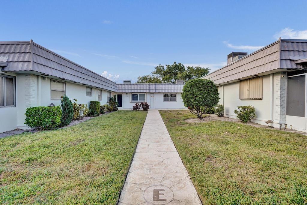 A concrete walkway leads between two single-story residential buildings with white walls and gray roofs — 108 Valencia Boulevard # E108, Delray Beach FL 33446, DELRAY BEACH, FL