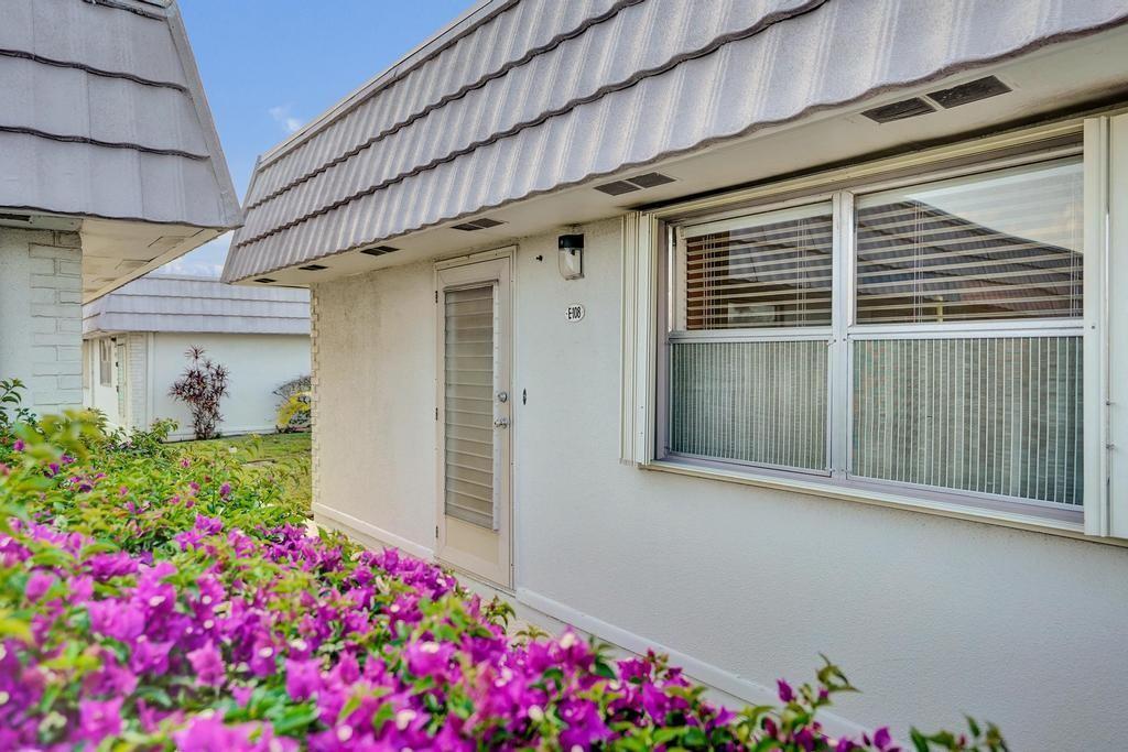 A white exterior building with a sloped roof, a door labeled E108, and purple flowers — 108 Valencia Boulevard # E108, Delray Beach FL 33446, DELRAY BEACH, FL