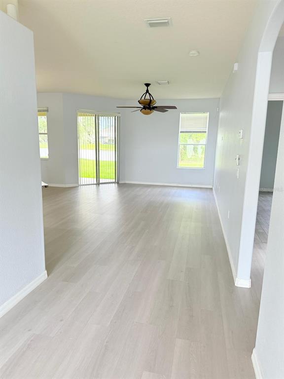 An open-concept living area features light-colored wood-look flooring, a ceiling fan, and sliding glass doors — 1905 FAIRWAY LOOP, KISSIMMEE, FL