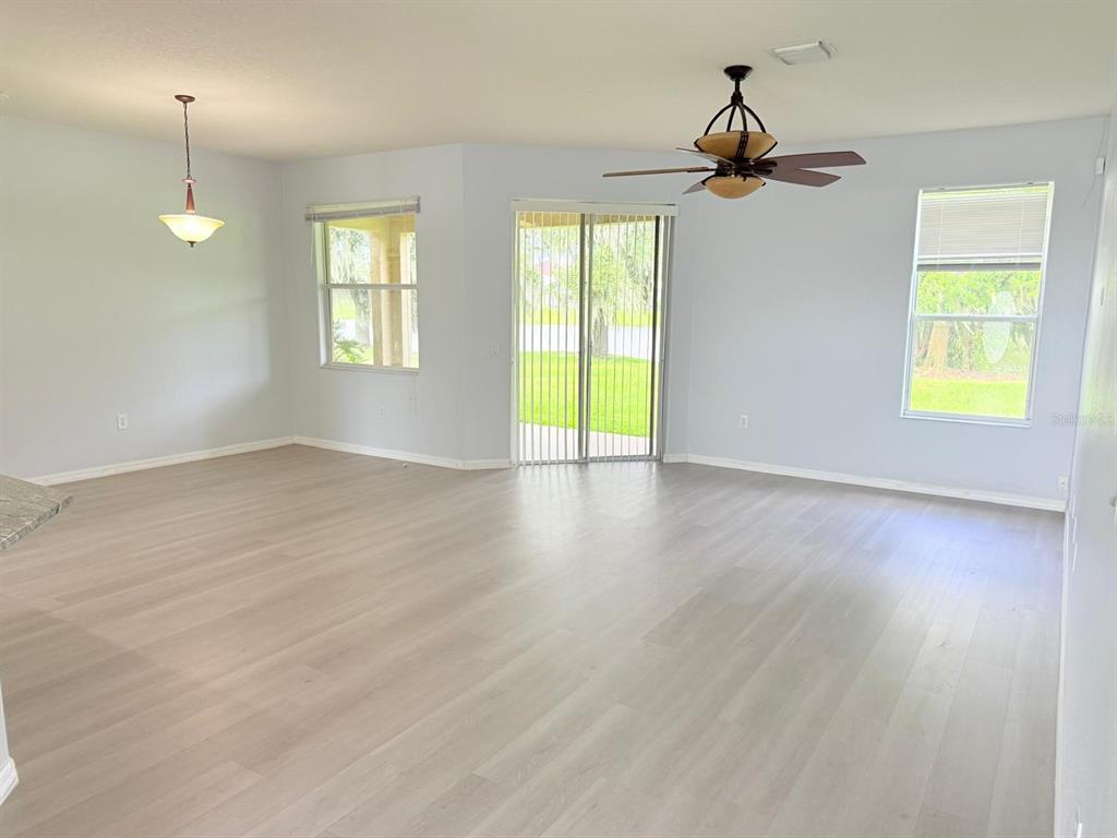 An open living area features light wood-look flooring, a ceiling fan, and sliding glass doors — 1905 FAIRWAY LOOP, KISSIMMEE, FL
