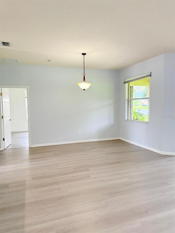 An empty room with light-colored walls, wood-look flooring, a hanging pendant light, and a window — 1905 FAIRWAY LOOP, KISSIMMEE, FL