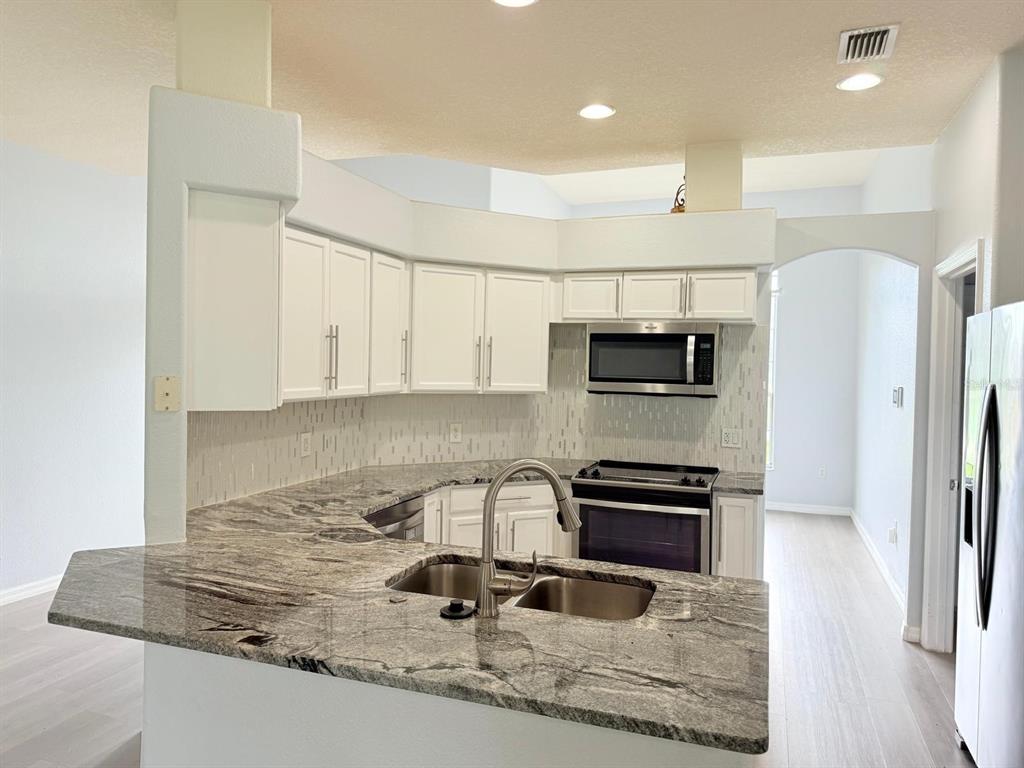 A kitchen features white cabinets, granite countertops, a stainless steel sink, and stainless steel appliances — 1905 FAIRWAY LOOP, KISSIMMEE, FL