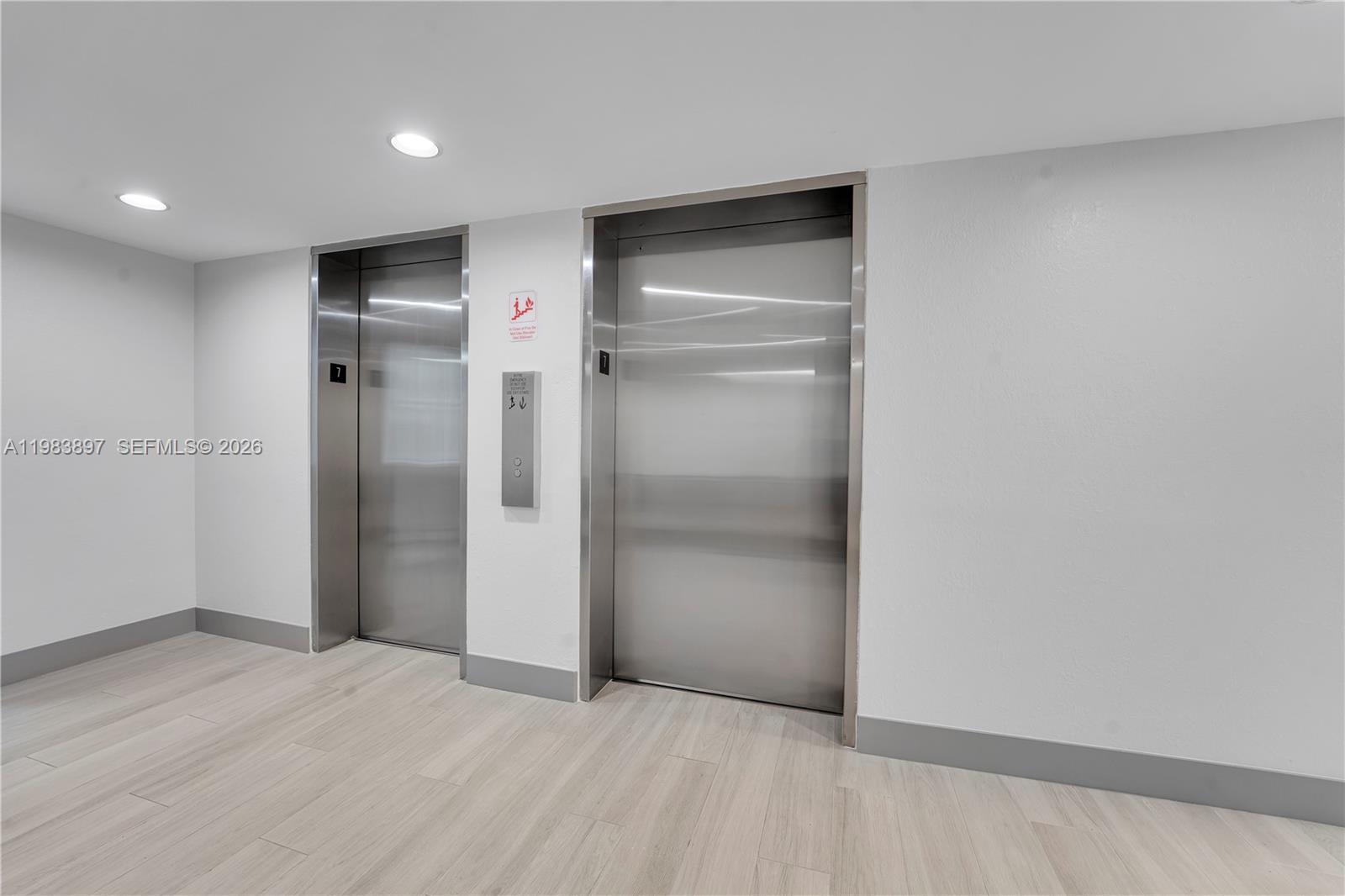 Two stainless steel elevator doors are set into a white wall with light wood flooring — 919 Hillcrest Dr # 210, Hollywood FL 33021, HOLLYWOOD, FL