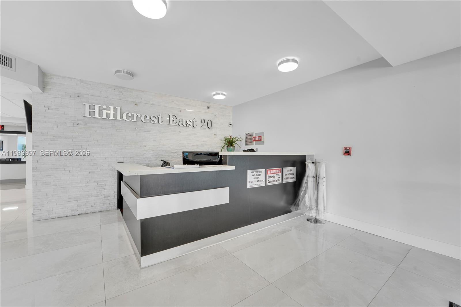 A modern reception desk sits in front of a white stone wall in a lobby — 919 Hillcrest Dr # 210, Hollywood FL 33021, HOLLYWOOD, FL