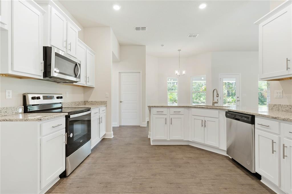 A kitchen with white cabinets, stainless steel appliances, granite countertops, and wood-look flooring — 338 UNDERWOOD TRAIL, PALM COAST, FL