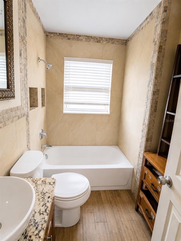 A bathroom features a white bathtub, a toilet, a vanity, and tan tiled walls — 3756 EDISON AVENUE, FORT MYERS, FL