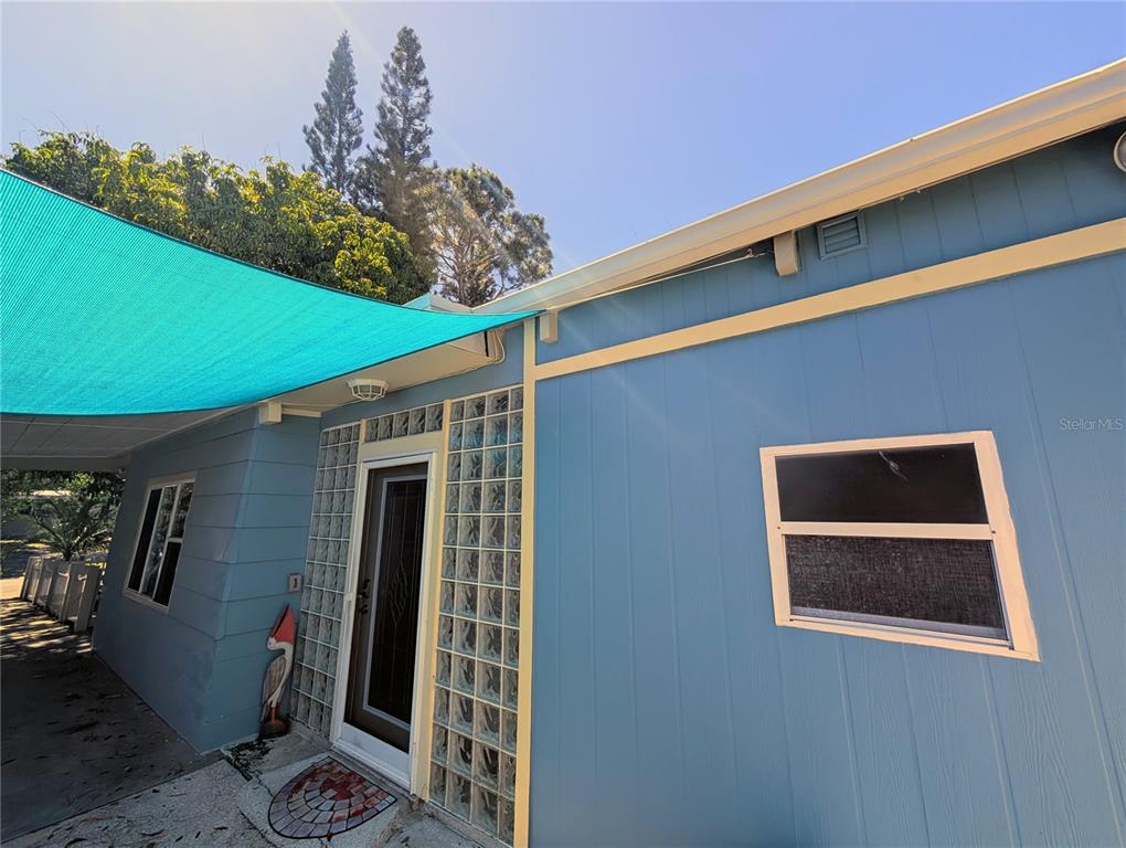 A blue house exterior features a covered carport with a turquoise shade sail and pond — 1519 CHANDLER AVENUE, CLEARWATER, FL