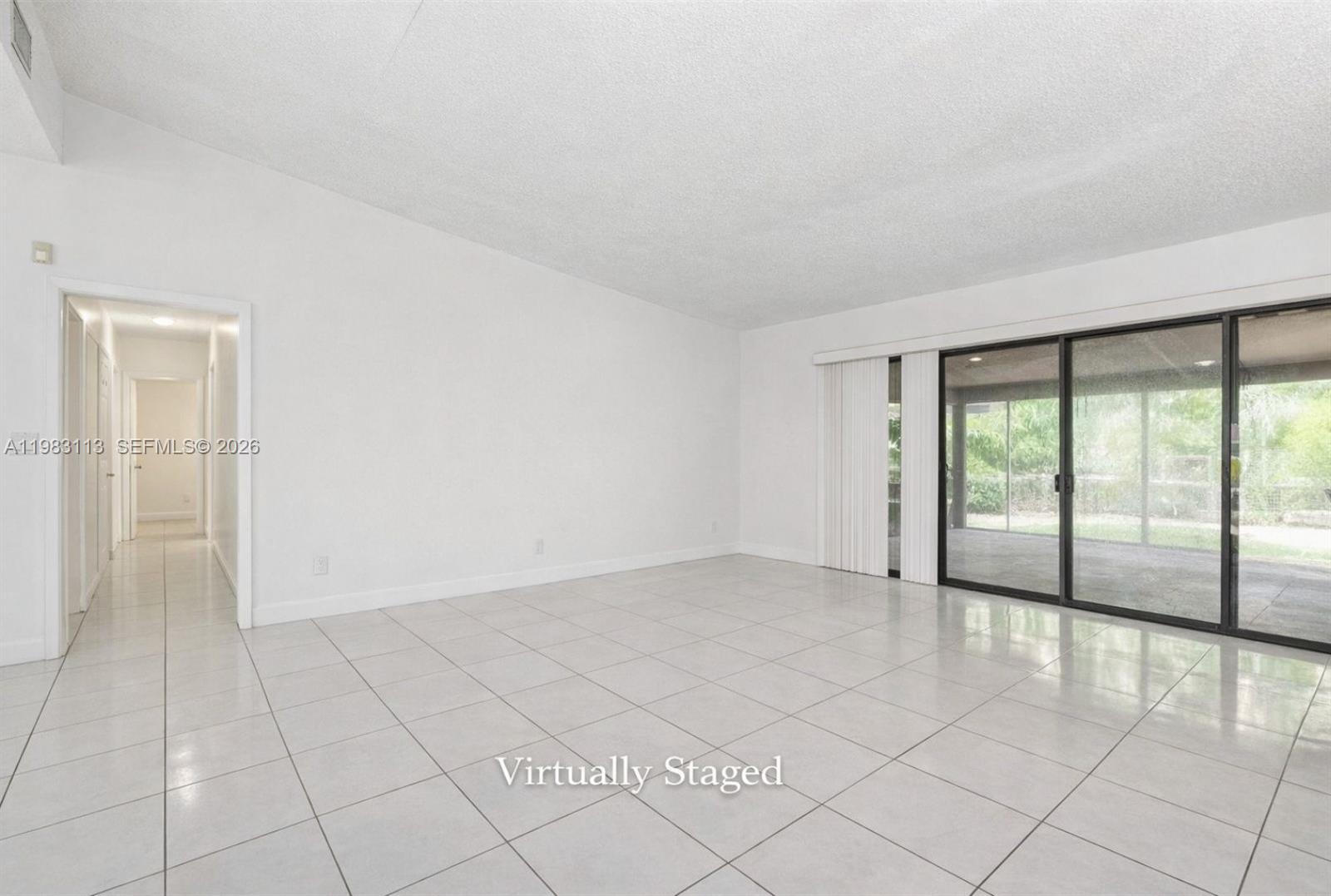 A bright, empty living room features white tile flooring, white walls, and large sliding glass doors — 550 NE 173rd St, North Miami Beach FL 33162, NORTH MIAMI BEACH, FL