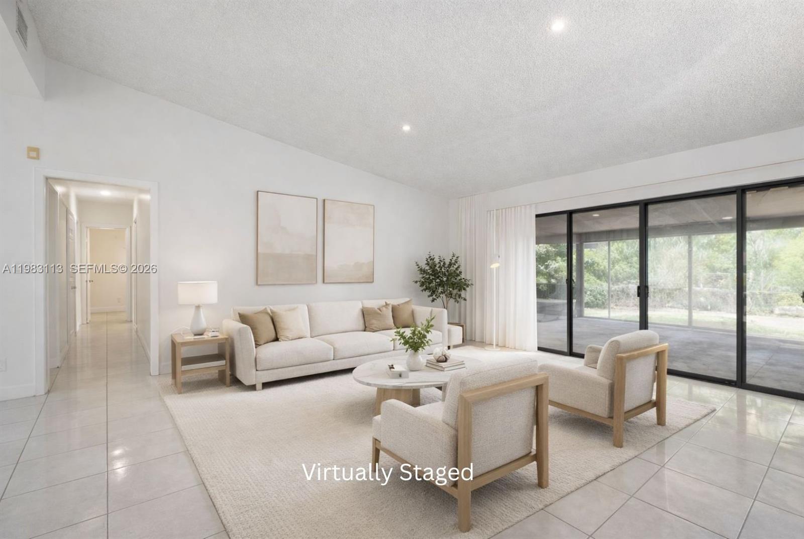 This virtually staged living room features white tile floors, a vaulted ceiling, and sliding glass doors — 550 NE 173rd St, North Miami Beach FL 33162, NORTH MIAMI BEACH, FL