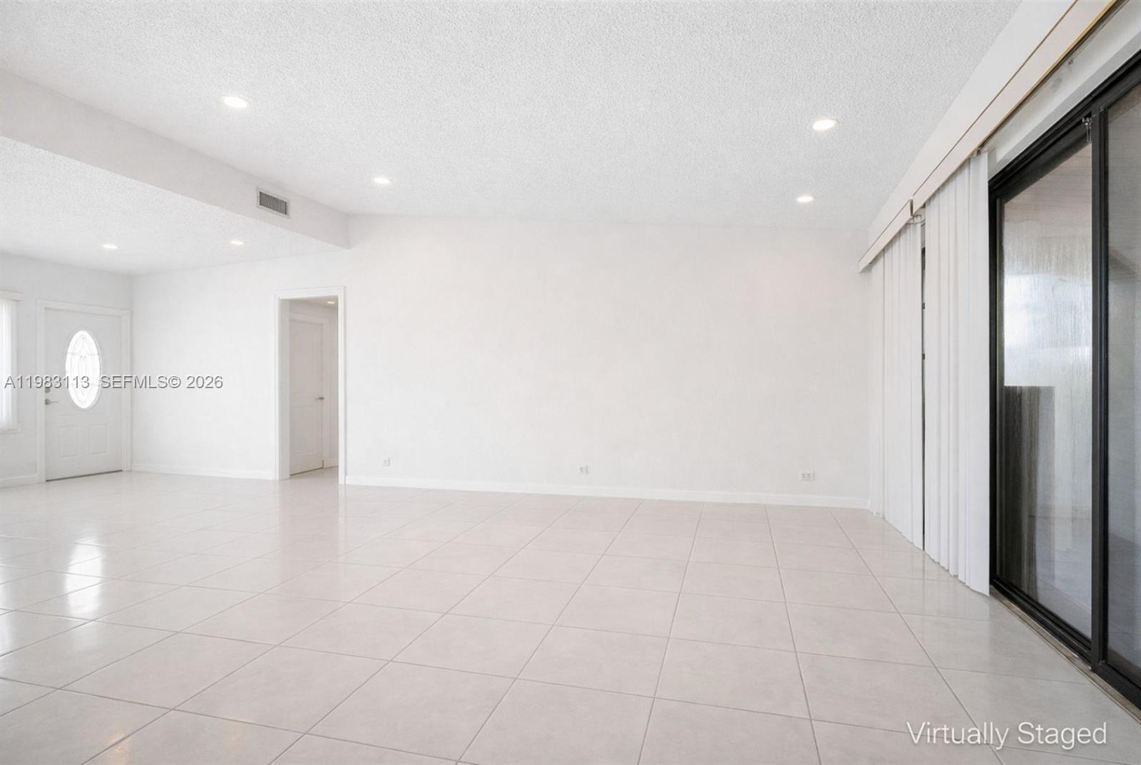 A bright, empty living room features white walls, light-colored tile flooring, and sliding glass doors — 550 NE 173rd St, North Miami Beach FL 33162, NORTH MIAMI BEACH, FL