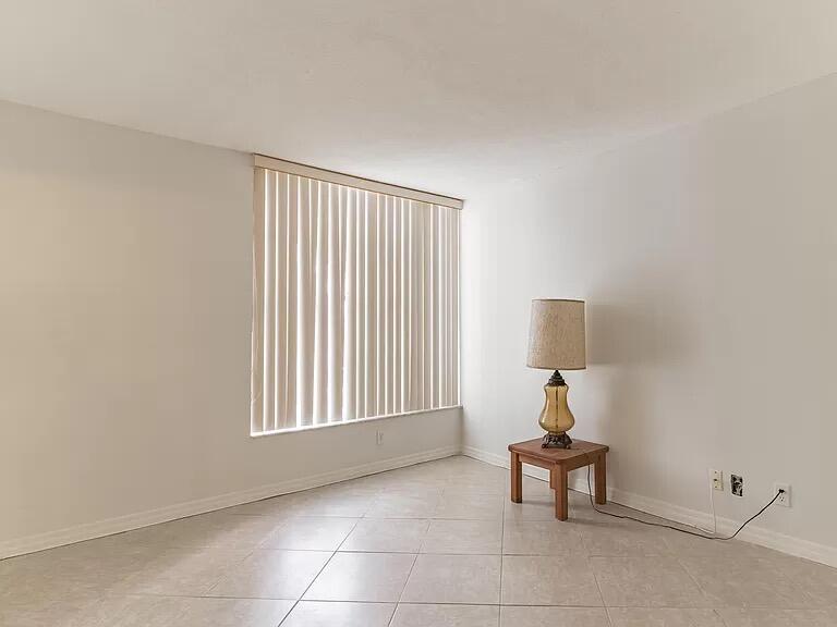 An empty room with light-colored tile flooring, white walls, vertical blinds, and a side table — 6901 Cypress Road # C14, Plantation FL 33317, PLANTATION, FL