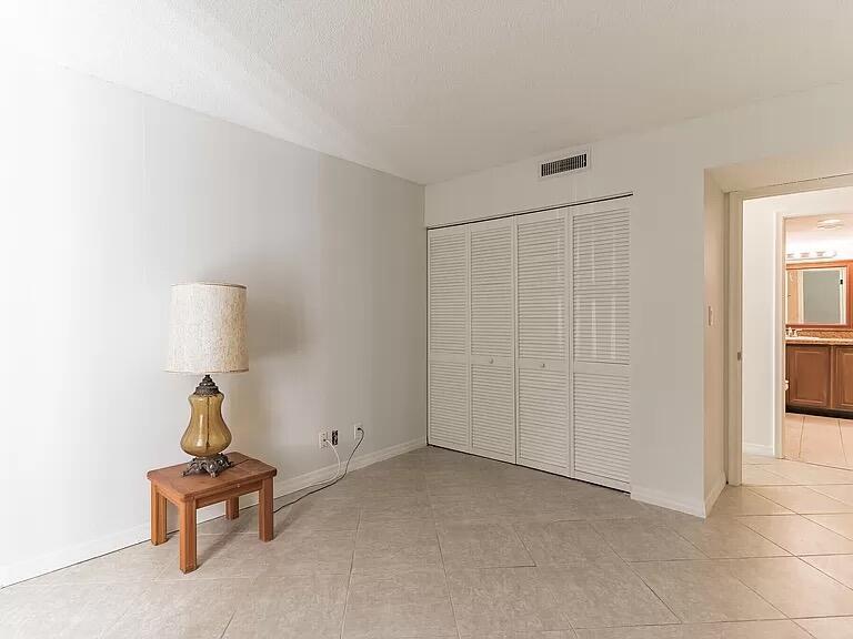 A room with light-colored tile flooring, a small wooden side table, and white closet doors — 6901 Cypress Road # C14, Plantation FL 33317, PLANTATION, FL