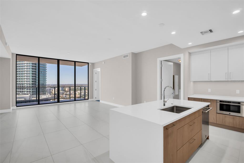 A modern kitchen with a white island and light wood cabinets opens to a living area — 275 1ST AVENUE S UNIT 2708, ST PETERSBURG, FL